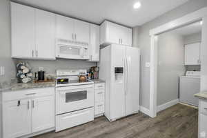 Kitchen featuring white appliances, white cabinetry, washer / dryer, dark wood-style flooring, and light stone countertops