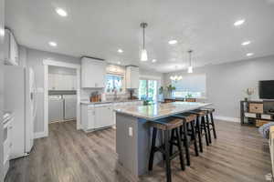 Kitchen featuring washer and dryer, white cabinets, light stone countertops, dark wood-type flooring, and a breakfast bar