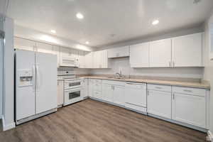 Kitchen with white appliances, white cabinets, dark wood finished floors, and recessed lighting