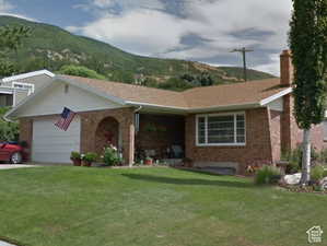 Ranch-style home with a front lawn, brick siding, a garage, and a chimney