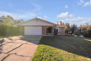 Single story home with brick siding, concrete driveway, a garage, a front yard, and a chimney