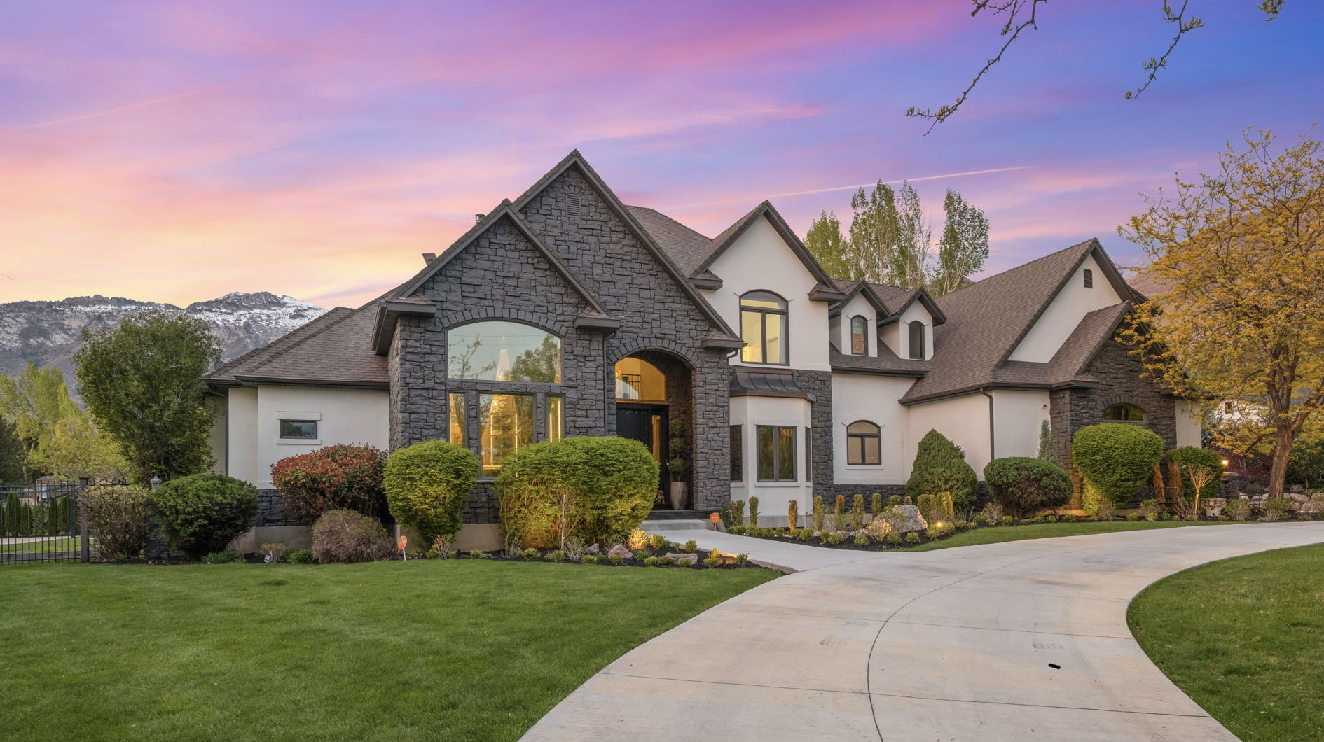 French country inspired facade featuring stone siding, a front yard, stucco siding, and curved driveway