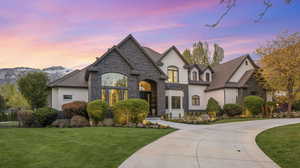 French country inspired facade featuring stone siding, a front yard, stucco siding, and curved driveway