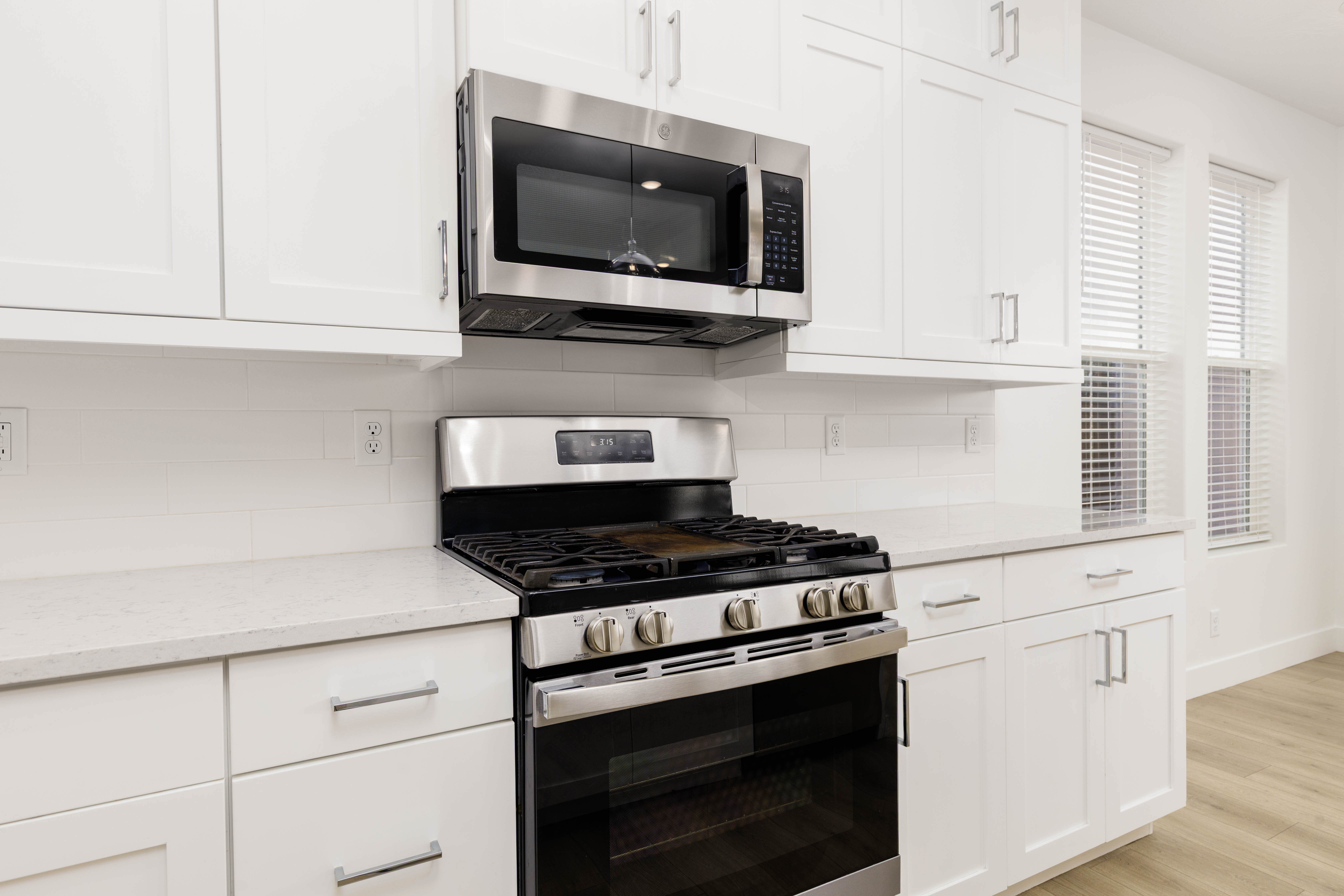Kitchen featuring stainless steel appliances, white cabinetry, light stone countertops, backsplash, and light wood-style flooring