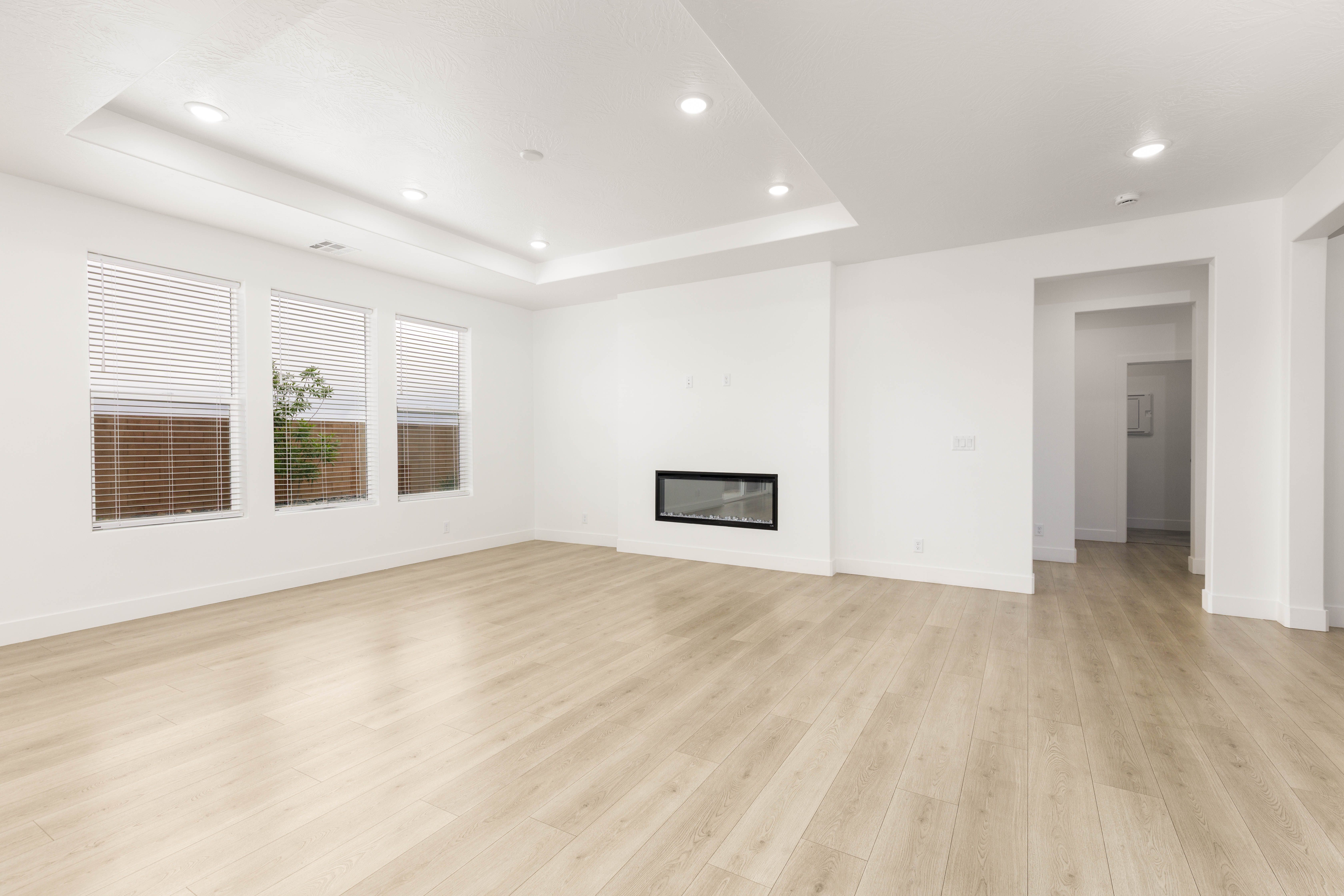 Unfurnished living room featuring recessed lighting, a glass covered fireplace, light wood-style floors, and a raised ceiling