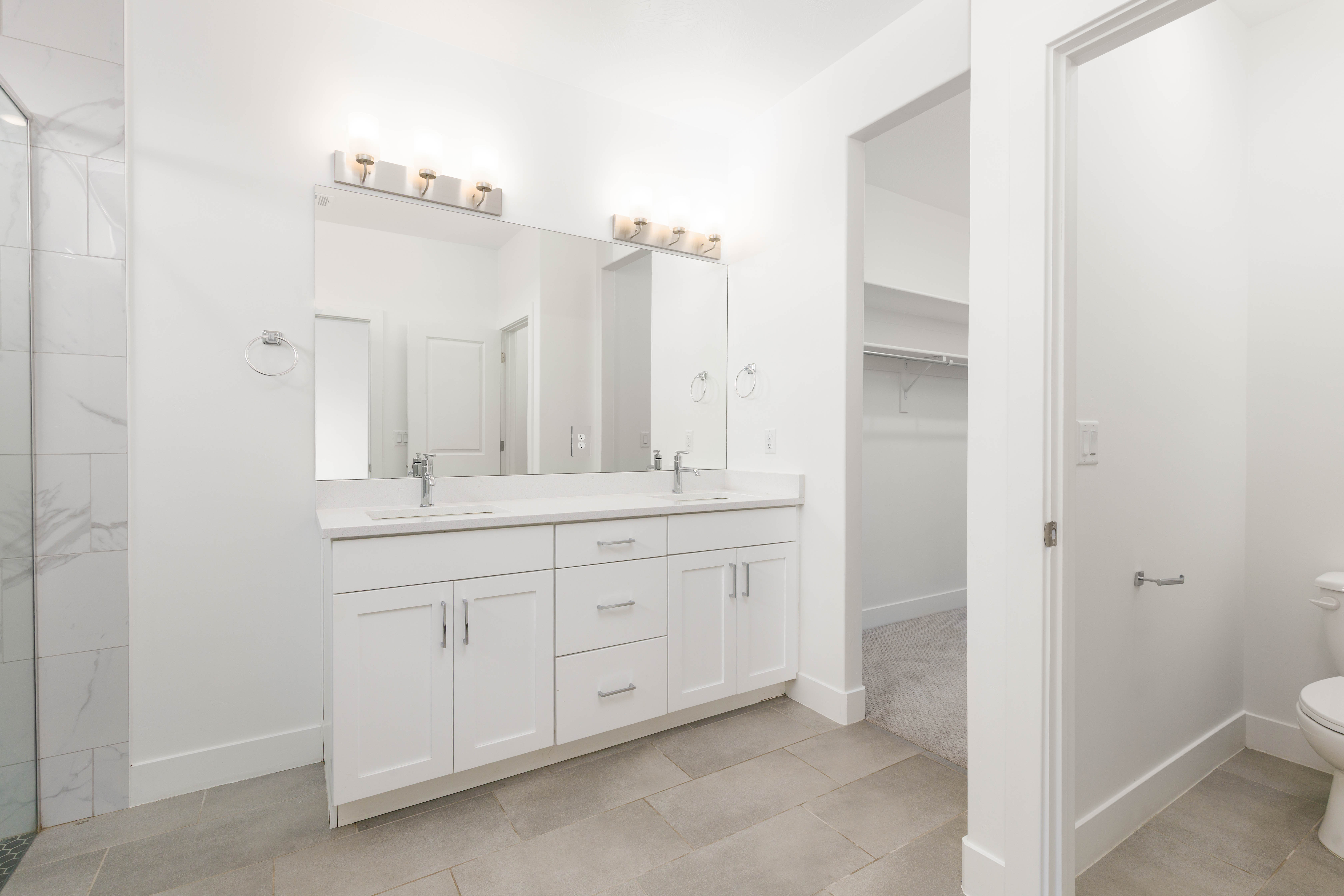 Full bathroom with double vanity, a walk in closet, and light tile patterned floors