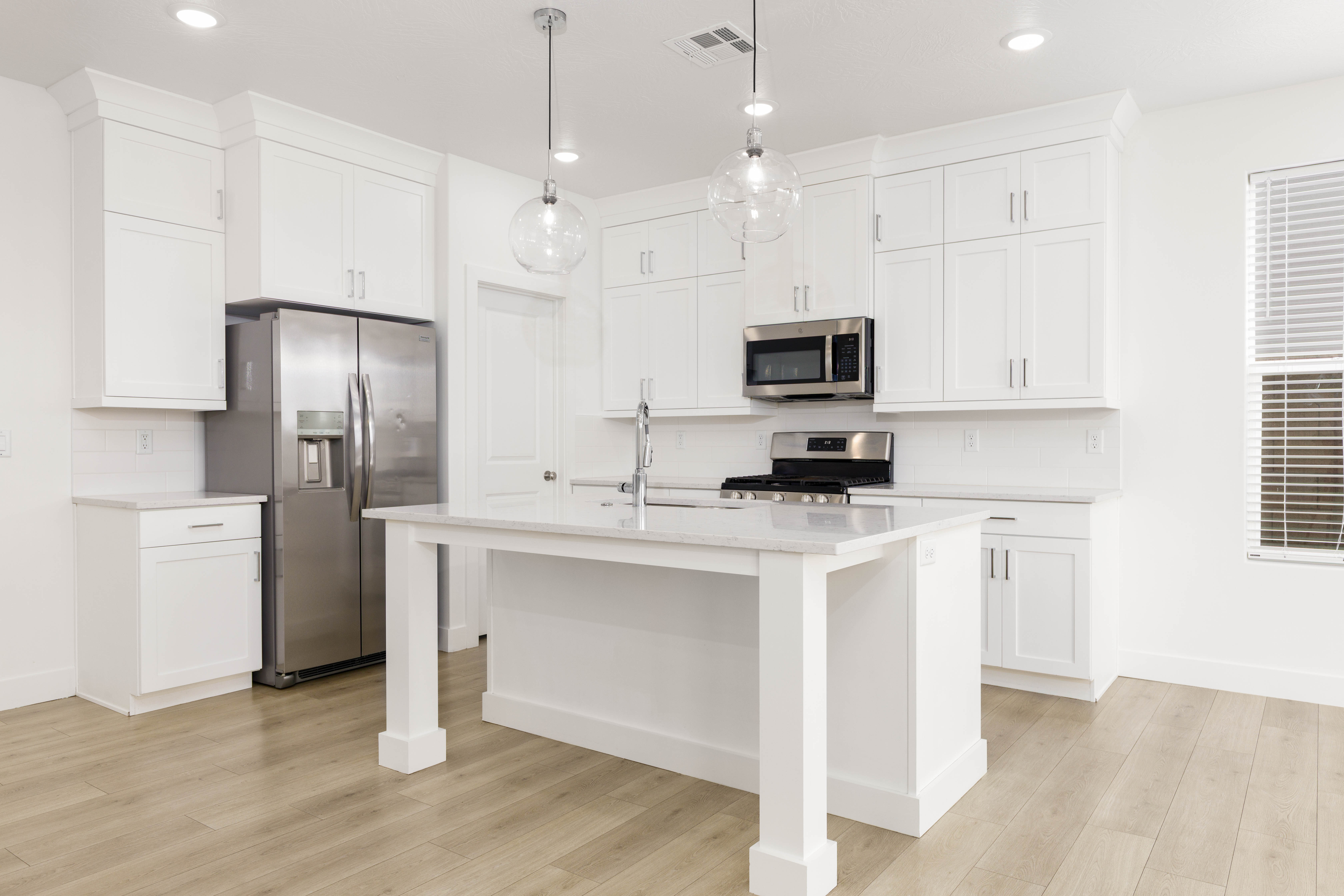 Kitchen featuring white cabinetry, stainless steel appliances, decorative backsplash, and light wood-style flooring