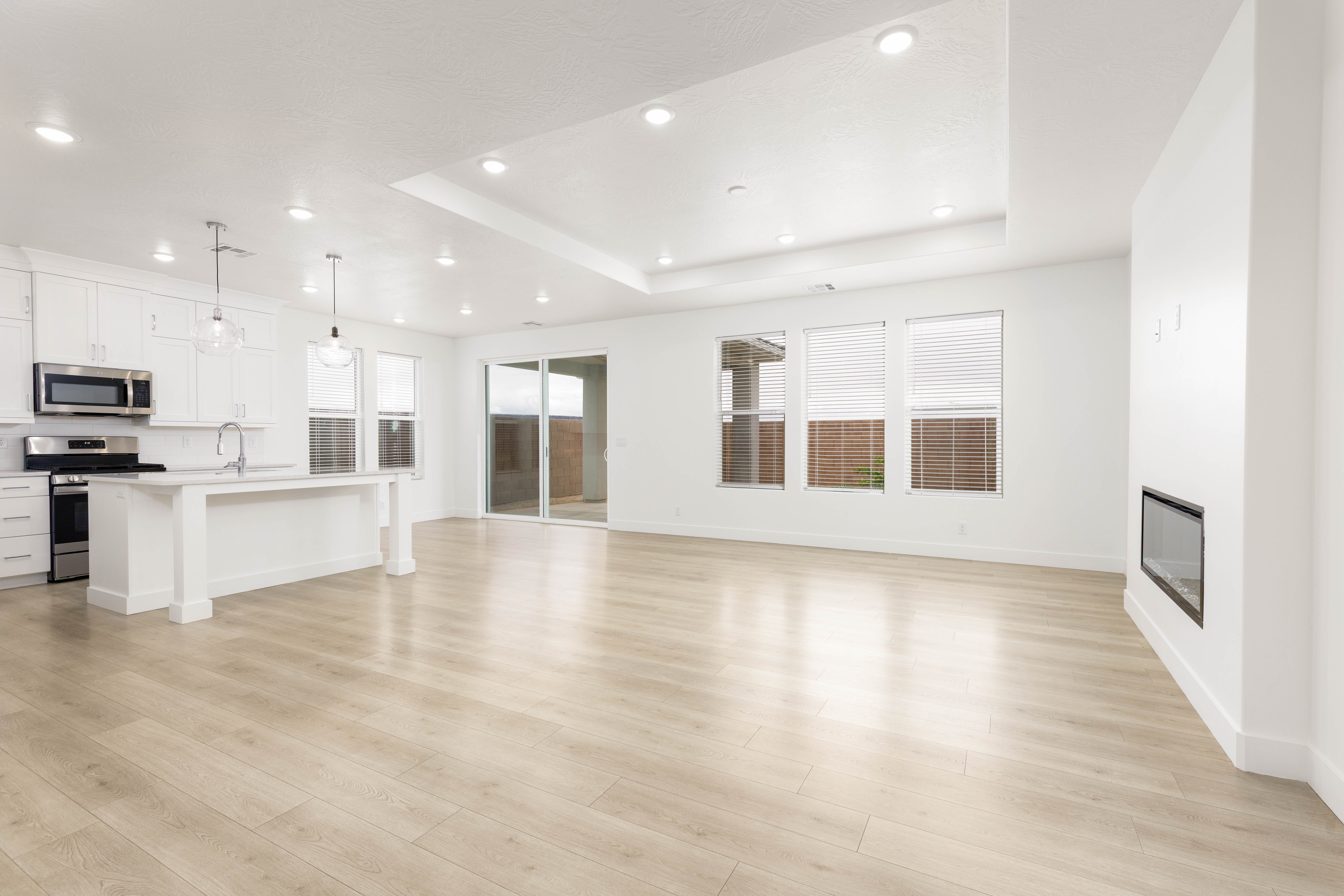 Unfurnished living room with a tray ceiling, recessed lighting, light wood-style flooring, and a glass covered fireplace