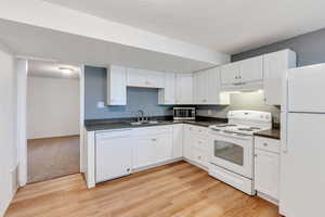 Kitchen with white appliances, dark countertops, light wood-style flooring, and white cabinetry