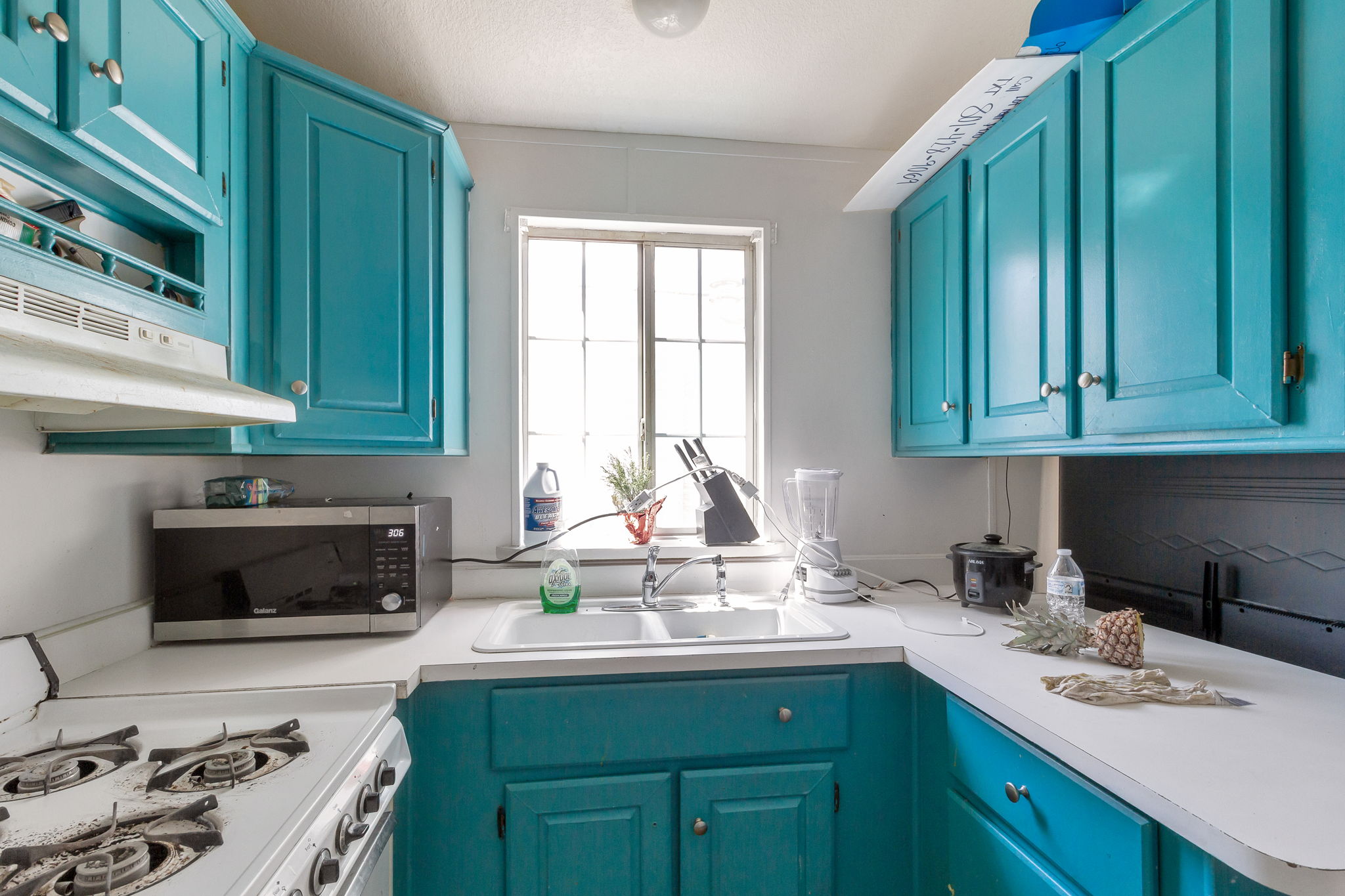 Kitchen with white gas range oven, light countertops, stainless steel microwave, and blue cabinets