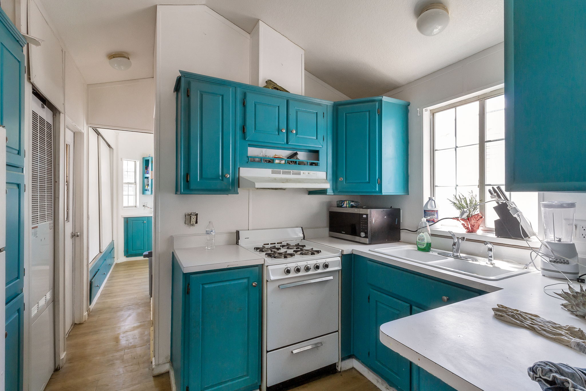 Kitchen featuring white gas range oven, light countertops, blue cabinets, stainless steel microwave, and vaulted ceiling