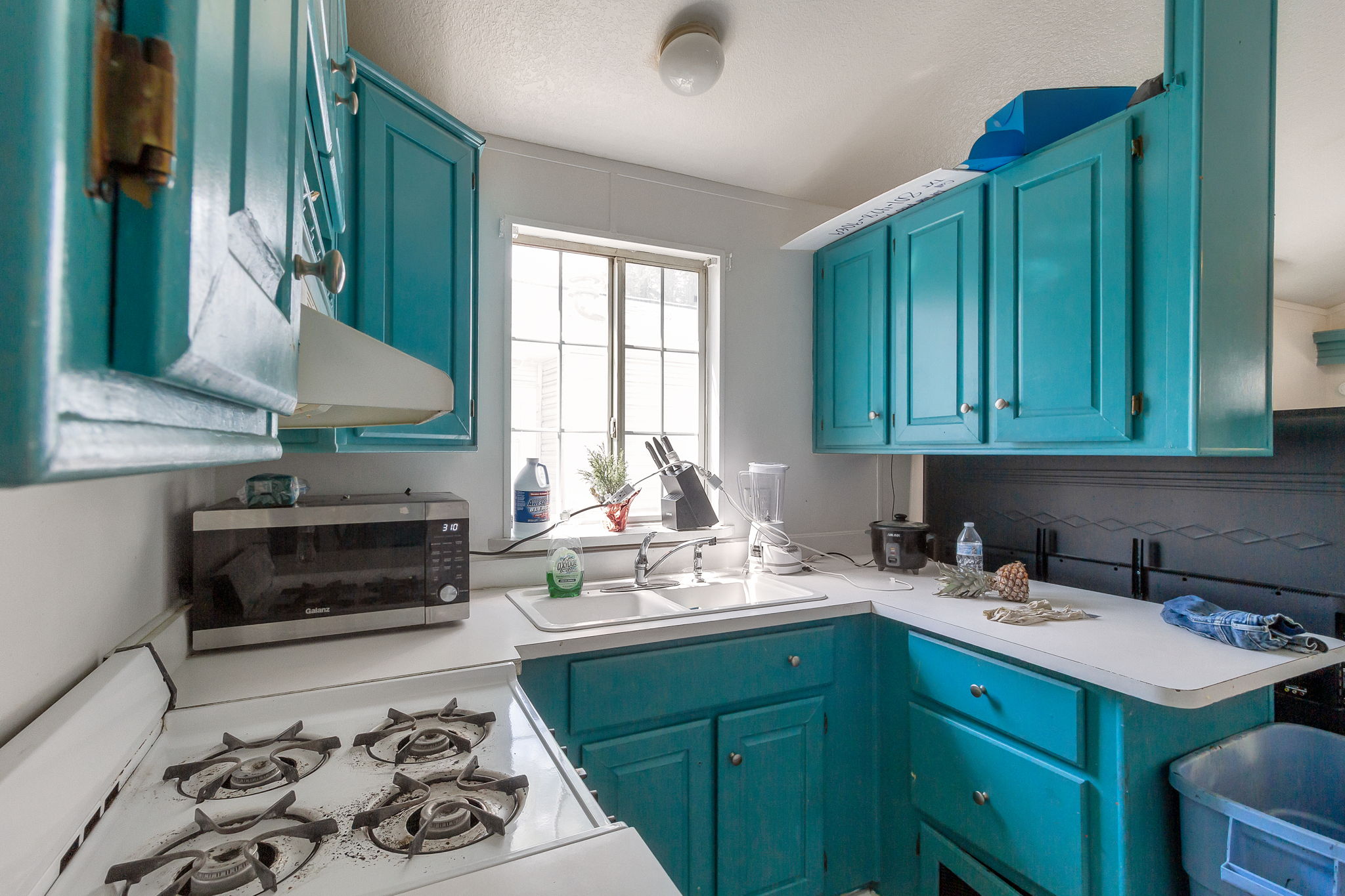 Kitchen with light countertops, white gas stove, stainless steel microwave, blue cabinets, and a textured ceiling