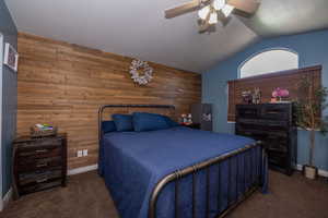 Bedroom featuring wood walls, dark colored carpet, lofted ceiling, ceiling fan, and an accent wall