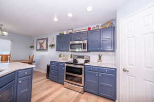 Kitchen featuring stainless steel appliances, blue cabinets, light wood-type flooring, and hanging light fixtures