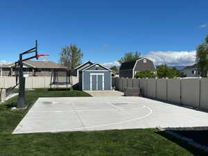 View of sport court with a storage shed, a fenced backyard, basketball hoop, and a trampoline