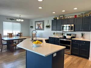 Kitchen featuring stainless steel appliances, decorative backsplash, light wood finished floors, light stone countertops, and a center island with sink