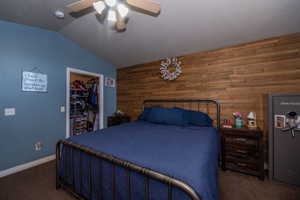Bedroom featuring wood walls, a spacious closet, dark carpet, vaulted ceiling, and ceiling fan