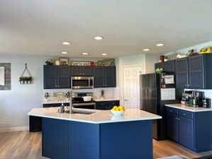 Kitchen featuring stainless steel appliances, light wood-style floors, tasteful backsplash, a center island with sink, and recessed lighting