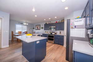 Kitchen with blue cabinetry, stainless steel appliances, an island with sink, backsplash, and light wood-type flooring