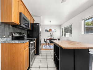Kitchen featuring stainless steel appliances, wood counters, decorative light fixtures, dark cabinets, and a kitchen island