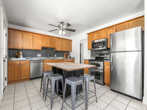 Kitchen featuring stainless steel appliances, a kitchen bar, wooden counters, decorative backsplash, and ceiling fan