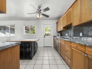 Kitchen with a ceiling fan, decorative backsplash, wood finish cabinetry, light tile patterned floors, and a textured ceiling