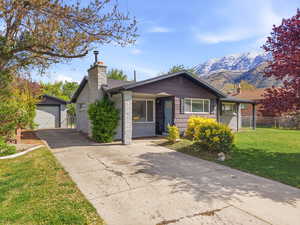 Single story home featuring a chimney, a front yard, an outbuilding, a garage, and driveway