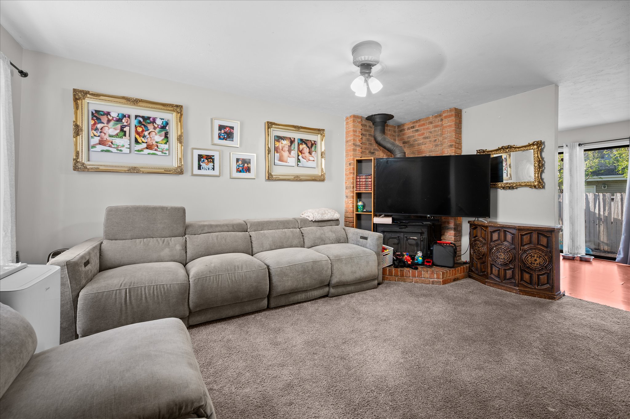 Carpeted living area with ceiling fan and a wood stove