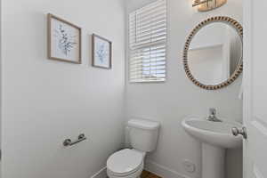 Half bathroom with toilet, pedestal sink, designer mirror, and LVP flooring