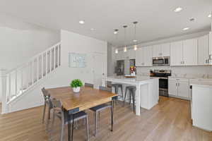 Kitchen with high ceilings, white cabinetry, spacious island, upgraded quartz countertops, LVP flooring, and stainless steel appliances