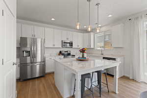 Kitchen with high ceilings, white cabinetry, spacious island, upgraded quartz countertops, LVP flooring, and stainless steel appliances