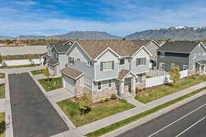 Exterior view of home featuring light Hardie board siding, stone, covered front porch, and a side-load garage.
