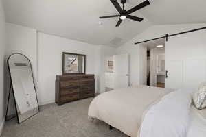 Primary bedroom with light colored carpet, vaulted ceiling, designer lighting, and barn-style door