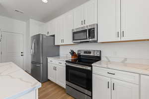 Kitchen with high ceilings, white cabinetry, spacious island, upgraded quartz countertops, LVP flooring, and stainless steel appliances