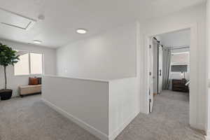Hallway and stairwell with light colored carpet and plenty of natural light