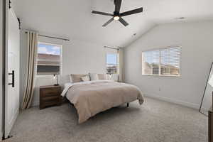 Primary bedroom with light colored carpet, vaulted ceiling, designer lighting, and barn-style door