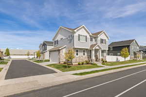 View of front of property with stone and Hardie board siding, covered front porch, and side-load garage