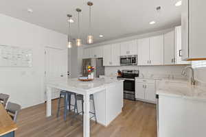 Kitchen with high ceilings, white cabinetry, spacious island, upgraded quartz countertops, LVP flooring, and stainless steel appliances