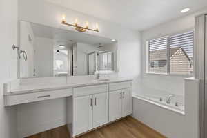 Primary ensuite bathroom featuring LVP flooring, vanity with white cabinets, upgraded quartz countertops, and makeup counter, separate soaker tub and shower
