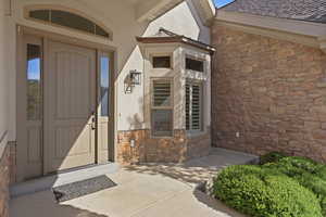 Doorway to property with stone siding, stucco siding, and roof with shingles