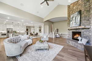 Living area featuring lofted ceiling, a fireplace, light wood finished floors, a ceiling fan, and arched walkways