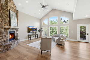 Living room featuring a high ceiling, a fireplace, light wood-style floors, a ceiling fan, and recessed lighting