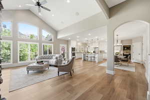 Living room with light wood-style floors, hanging lights, lofted ceiling, ceiling fan, and arched walkways