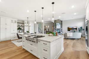 Kitchen with white cabinets, light wood-style floors, glass insert cabinets, and open floor plan