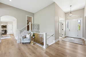 Foyer featuring hanging lights, light wood-style floors, arched walkways, and lofted ceiling