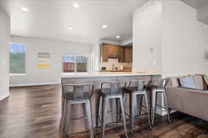 Kitchen featuring a peninsula, light countertops, open floor plan, a breakfast bar area, and dark wood-style flooring