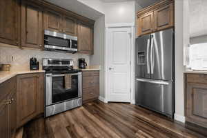 Kitchen featuring stainless steel appliances, dark wood finish cabinetry, dark wood-type flooring, tasteful backsplash, and light stone counters