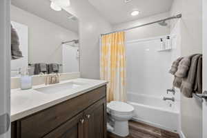 Bathroom featuring vanity, shower / bathtub combination with curtain, and dark wood-type flooring
