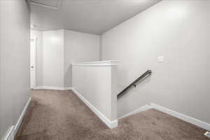 Corridor with an upstairs landing, carpet floors, and a textured ceiling