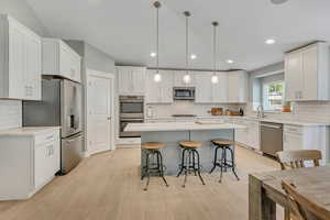 Kitchen with a breakfast bar, stainless steel appliances, decorative light fixtures, white cabinetry, and a kitchen island